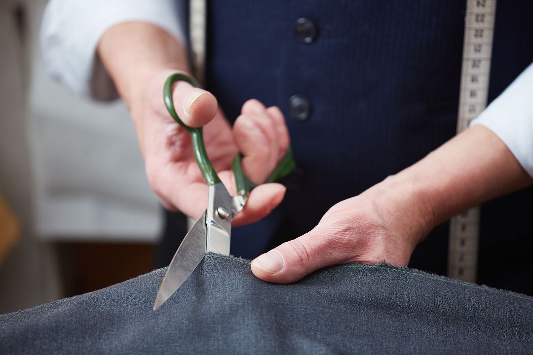 Hands of tailor with scissors cutting fabric